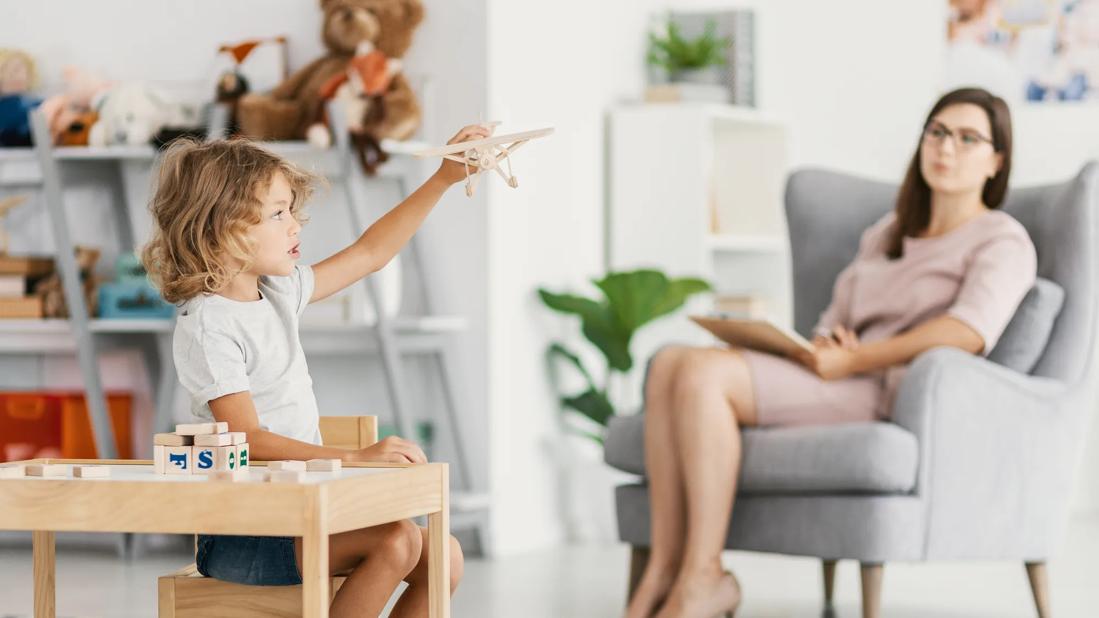 Child playing with toys, being assessed from afar by a healthcare provider