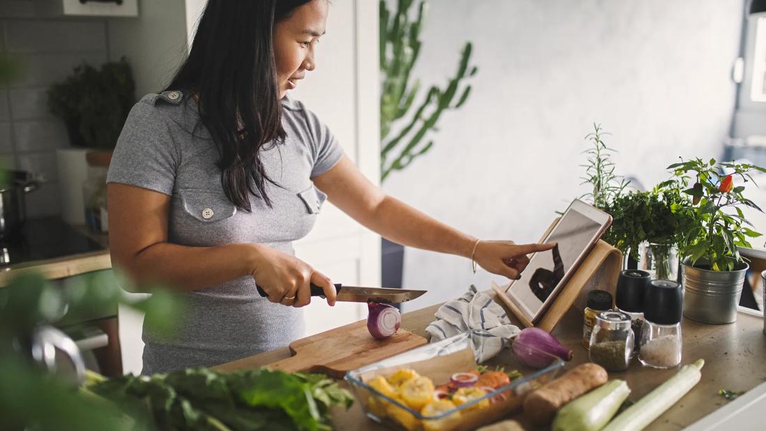 Person looking at a recipe on tablet in kitchen, using healthy, nutritional ingredients
