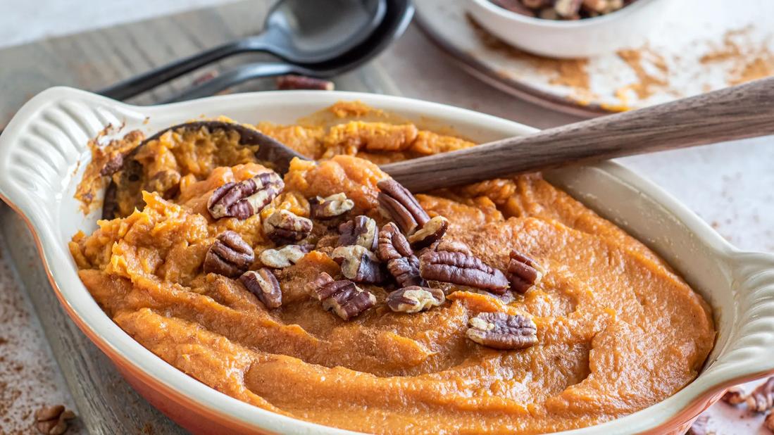 Ceramic serving dish with sweet potato mash with pecans on top, with wooden spoon