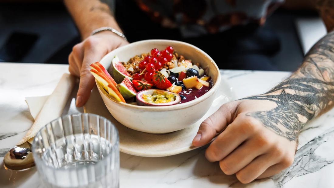 Person at table with a bowl filled with fruits and grains