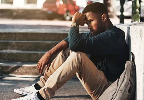 Stressed college student sitting on ground with head in hands.