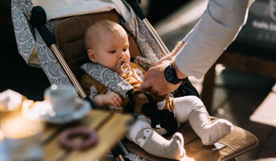 Baby with pacifier sitting in stroller, being strapped in