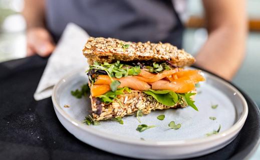 A salmon and greens sandwich on whole-grain bread being served on a plate