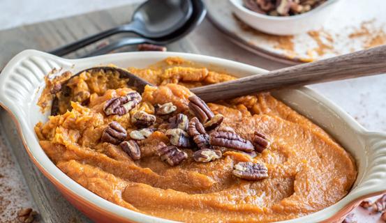 Ceramic serving dish with sweet potato mash with pecans on top, with wooden spoon