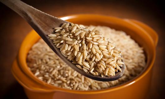 Wooden spoonful of brown rice over a slow cooker full of brown rice